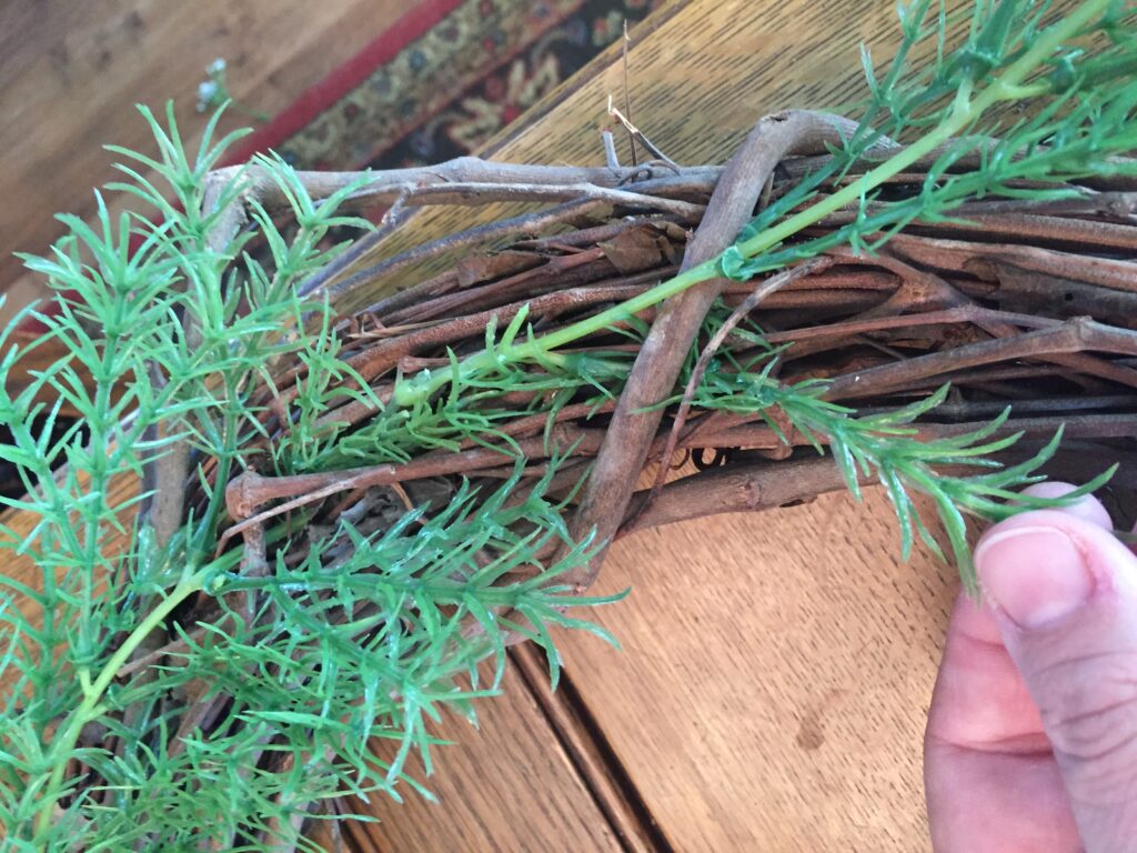 DIY farmhouse wreath, greenery being threaded under the grapevine twigs for security